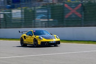 Yellow racing car sports car Porsche 911 GT3 RS races at high speed top speed during trackday on start-finish straight start-finish of race track