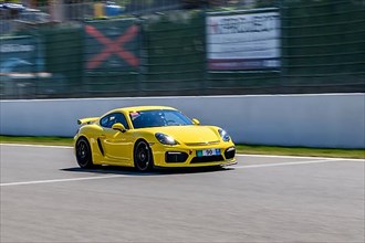 Yellow racing car sports car Porsche Cayman GT4 races at high speed top speed during trackday on start-finish straight of race track