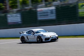 Racing car sports car Porsche Cayman GT4 races at high speed full throttle on start-finish straight of race track