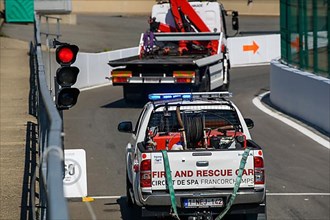 Tow truck and rescue vehicle drive through exit from pit lane onto race track at red lights due to race stoppage