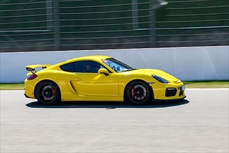 Yellow racing car sports car Porsche Cayman GT4 races at high speed top speed during trackday on start-finish straight of race track