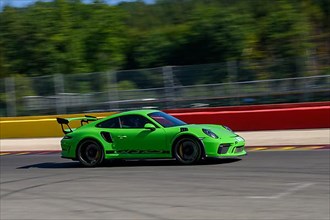 Green racing car sports car Porsche 911 GT3 RS races at high speed full throttle at exit of curve hairpin La Source of race track