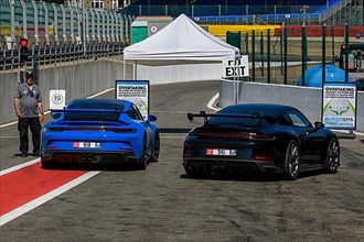 Two Porsche GT3 sports cars waiting at red lights at pit lane exit for clearance to enter race track
