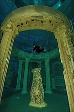 Diver dives over stylised ruins of antique temple at a depth of 20 metres in indoor diving tower