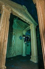 Diver dives through stylised ruin of portal entrance of ancient temple in 20 metres water depth in indoor diving tower