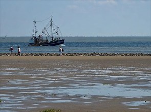 A fishing boat passes close to the beach inland through the Wadden Sea of the North Sea at the mouth of the Elbe