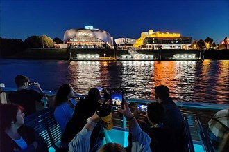 People on the harbour ferry photographing the Stage Theater with the Elbe in the evening