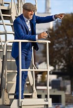 Man in blue suit with bow tie and binoculars stands at the harbour
