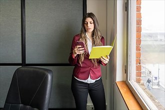 Young blonde business woman in her office using the phone while checking notes