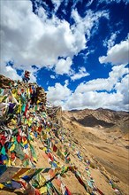 Travel photographer taking photos in Himalayas mountains on cliff with Buddhist prayer flags. Leh