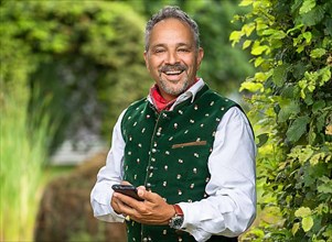Happy laughing man in Bavarian traditional costume with mobile phone in hand