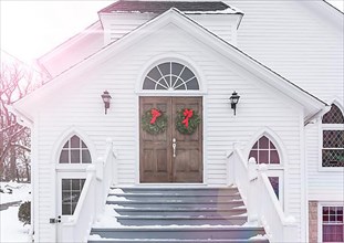 Christmas wreaths hang from entrance doors of rustic church in winter snow scene