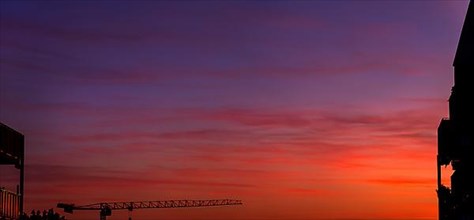 Construction crane in front of red-blue sky at sunset