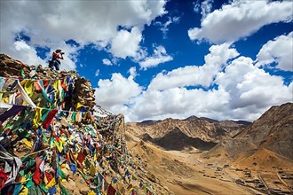 Travel photographer taking photos in Himalayas mountains on cliff with Buddhist prayer flags. Leh