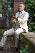 Man in suit sitting on a wall and looking strained into his phone