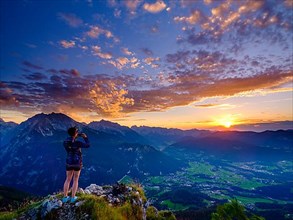 Mountaineer taking pictures of sunset with mobile phone