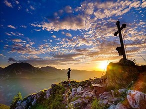 Mountaineer standing at sunset at the summit cross of the Brettgabel