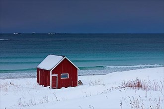 Red insulated wooden hut along the coast in the snow in winter