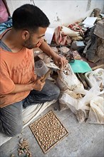 Moroccan cellular craftsman at work: hammering small pieces out of a tile