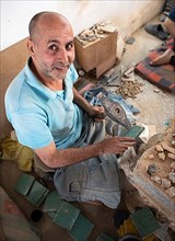 Moroccan cellular craftsman at work: hammering small pieces out of a tile