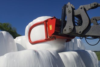 Plastic wrapped round silage bales stacked on a pile with mechanical loader