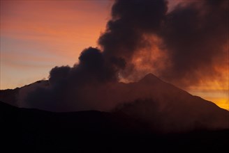 Smoke rising from volcano at sunset