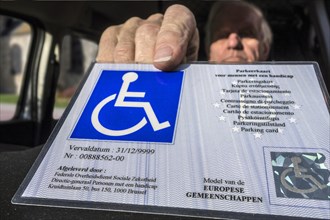 Disabled elderly man puts EU parking card for people with disabilities