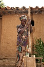 Woman beating cassava with a stick into a wooden pot to make flour
