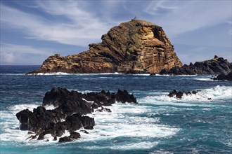 Rocks unswept by surf at the back small rocky island Ilheu Mole with lighthouse Farol do Porto Moniz