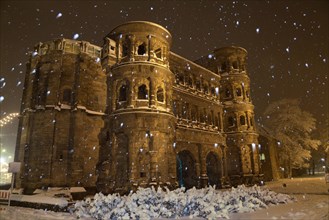 Roman city gate illuminated during snowfall at night