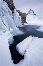 Kirkjufell mountain and the frozen waterfall Kirkjufellsfoss on Snaefellsnes peninsula in the snow in winter
