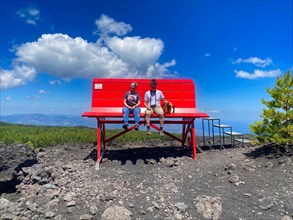 2 people sitting on huge red bench