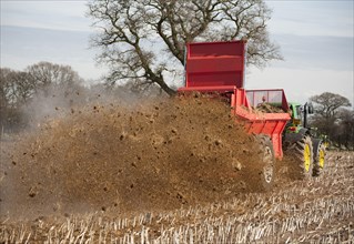 Tractor with manure spreader applying farmyard manure to maize stubble field