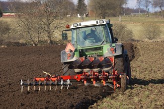 Tractor pulling a four-furrow reversible plough and a small harrow