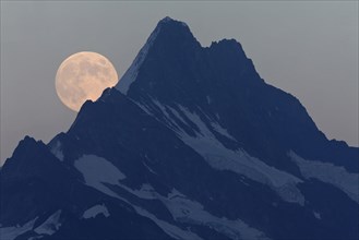 Full Moon rising over mountain peak at dusk