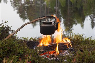 Blackened tin kettle boiling water over the flames of the campfire during a hike by the lake