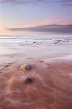 View of pebbles on beach with incoming tide at sunset