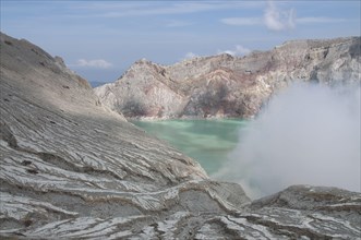 Turquoise-green coloured acidic volcanic crater lake with steam rising from its vent