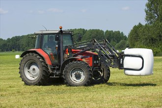 Massey Ferguson 6290 tractor with mechanical loader transporting plastic wrapped silage round bales