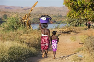 Malagasy daughter and mother carrying a laundry basket on their heads while walking along the Tsiribihina River