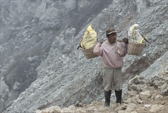 Local man carrying sulphur blocks in baskets on the slopes of the volcanic crater