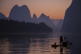 Traditional fisherman with trained cormorants standing on a bamboo raft at sunrise on a river in the karst area