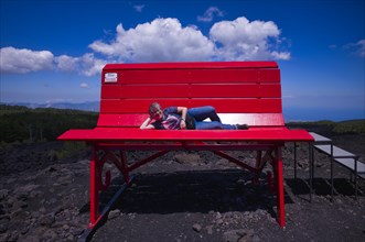 Elderly woman lying on huge red bench