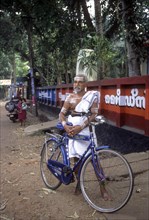 A Priest applying holy ash on body standing with bicycle