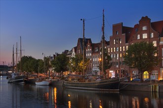 Museum harbour at night with traditional sailing boats moored on the Untertrave in the Hanseatic City of Luebeck