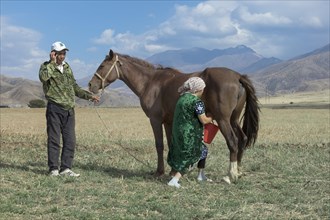Kazakh man with mobile phone and Kazakh woman milking a mare