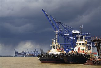 Tugboats moored at harbour of container port with passing rainclouds