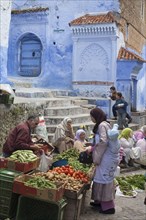 People at the market next to blue houses in the city
