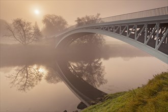View of river and cast iron road bridge in morning mist