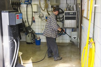 Dairy farmers clean milking parlour with high-pressure cleaner after morning milking